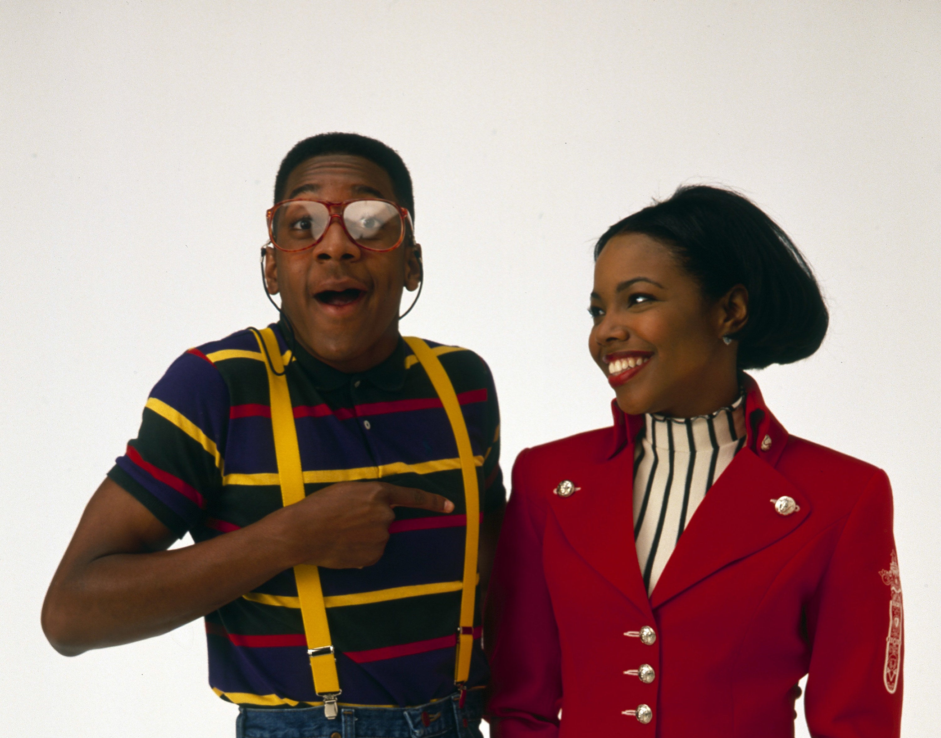 Photo of Urkel in a striped polo and yellow suspenders pointing to Laura wearing a red blazer