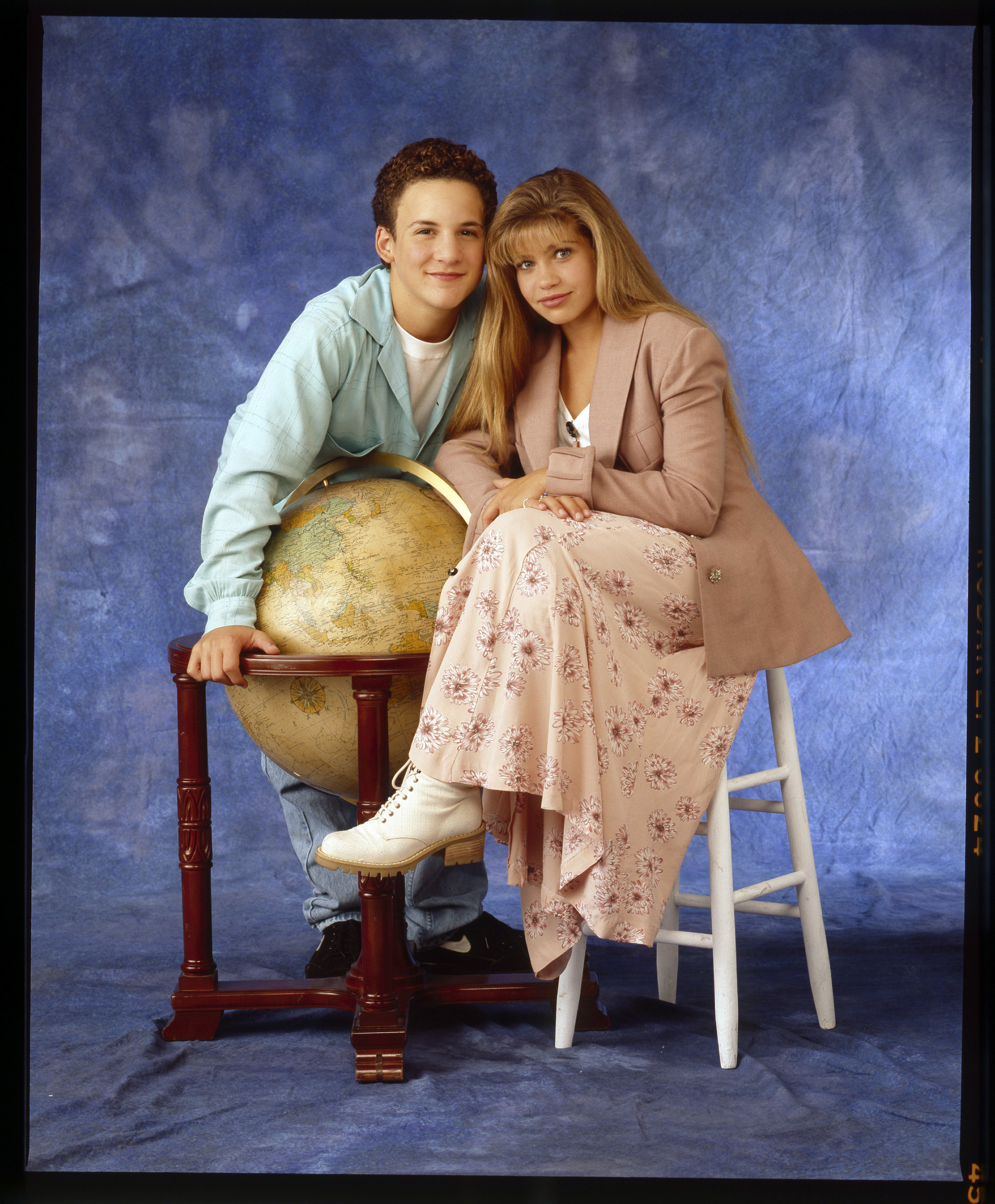 A photo of Cory and Topanga leaning on a globe with a tie-dye blue background