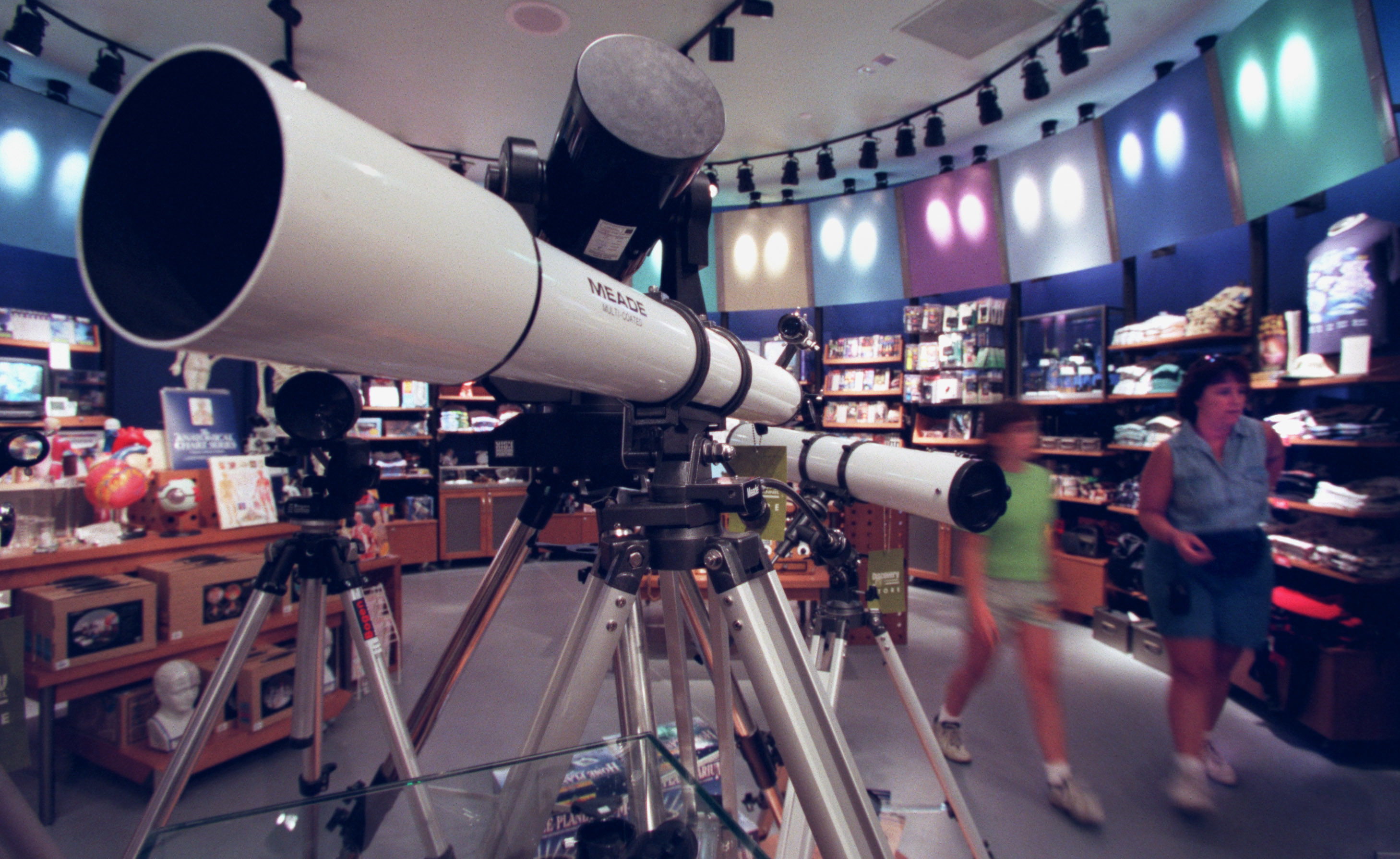 A telescope in the back of a store with shirts on the shelves behind it