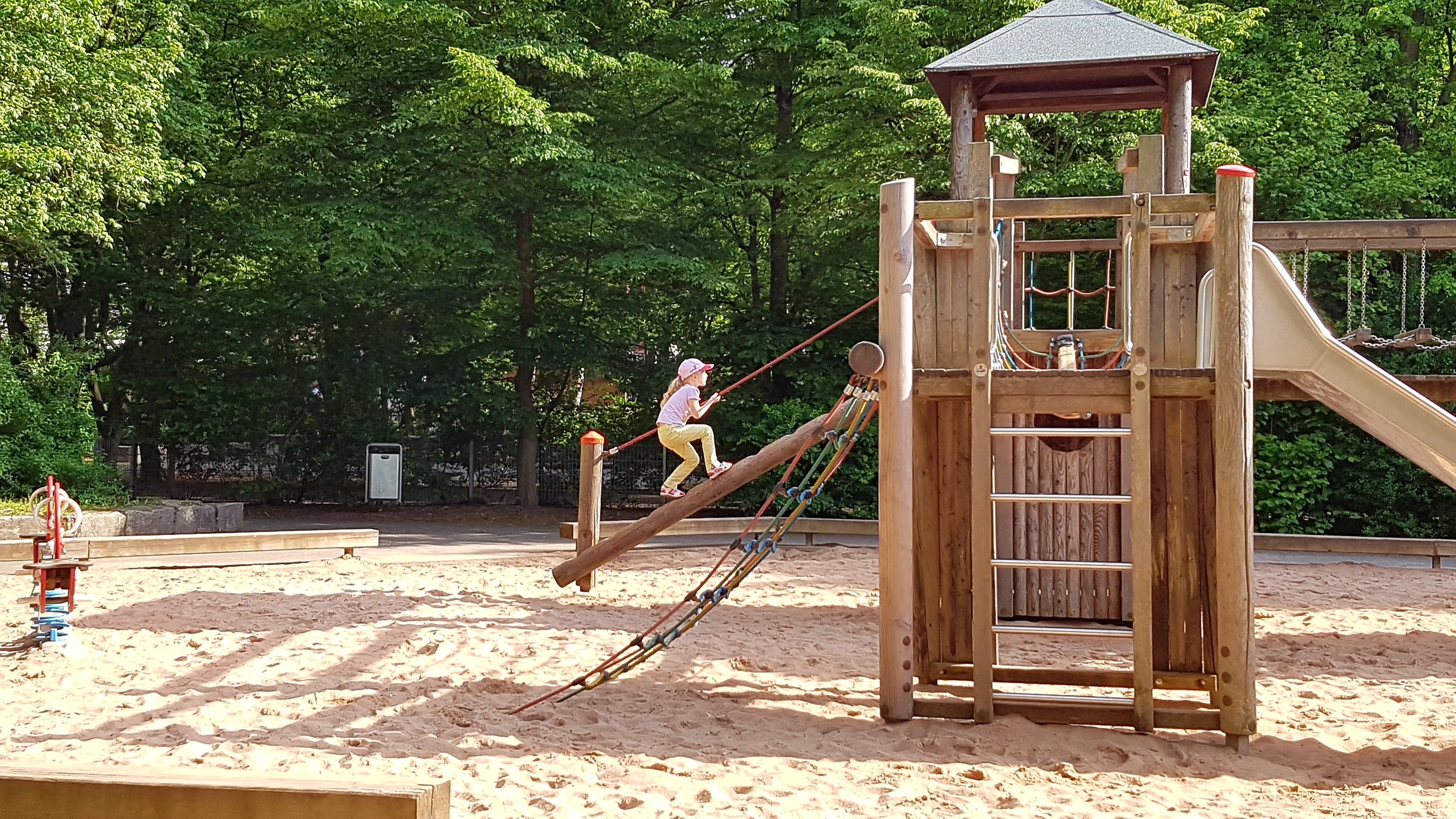 Photo of a girl climbing up the rope log of a wooden playground 