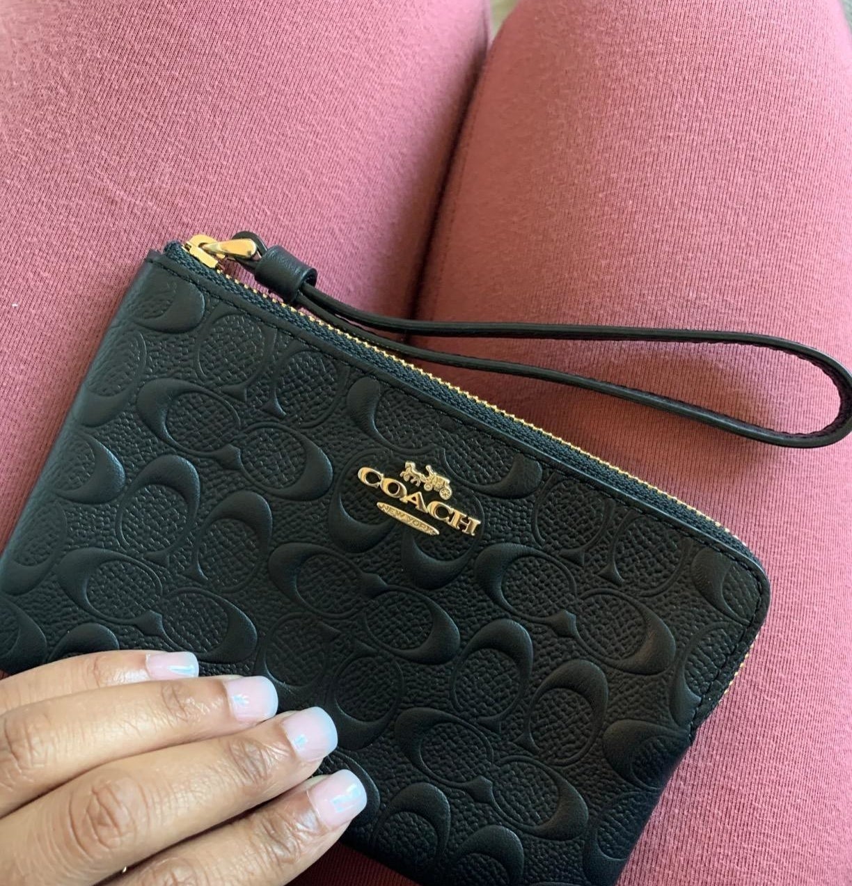 a reviewer&#x27;s photo of the black wristlet which has gold Coach branding