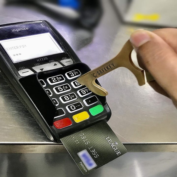 A person using the no-touch tool to operate a debit/credit card machine.