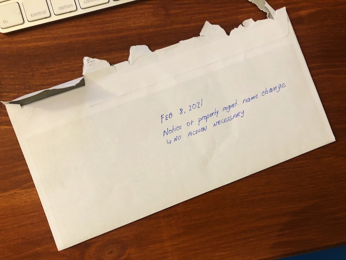 White envelope on desk with handwritten note on center reading, "Feb. 8, 2021. Notice of property management name change. No action necessary"