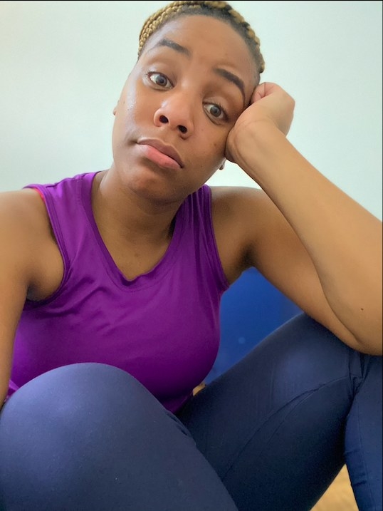 A woman in workout attire looks tired as she sits on the floor