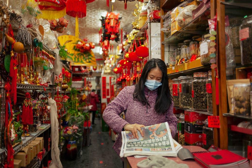 A woman wearing a mask and reading a newspaper in a store in Chinatown