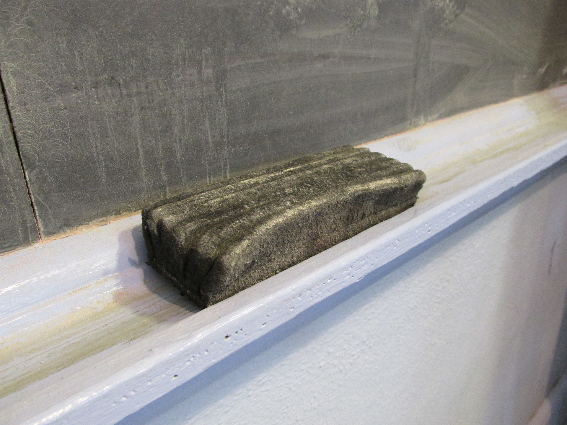 A dusty chalkboard eraser rests on a ledge beneath a chalkboard