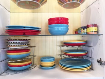 A reviewer photo of a cabinet with two of the shelves in each corner with plates stacked on each tier 