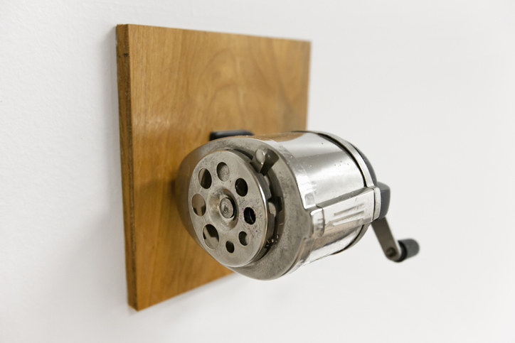 Old-fashioned wall-mounted pencil sharpener with a crank handle on a wooden block