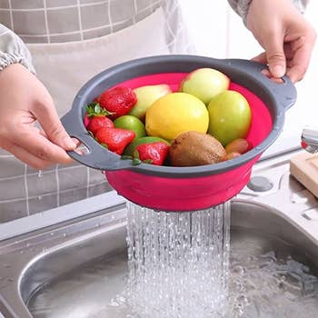 A pair of hands holding one of the colanders filled with vegetables and draining water 