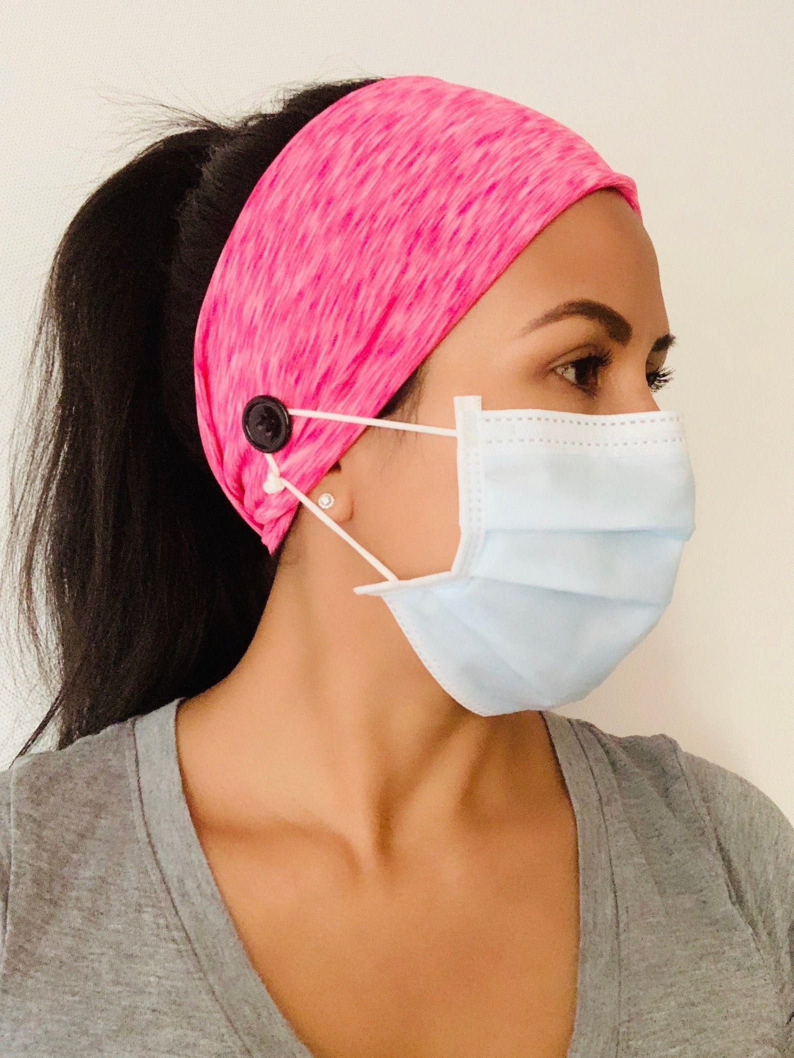 Model wearing a pink over the ear headband with a button on the side for attaching a mask strap 