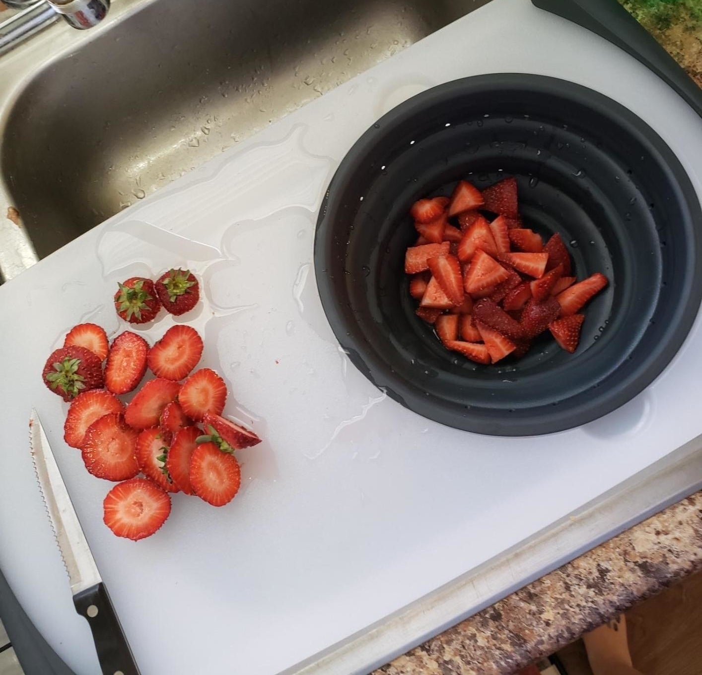 A reviewer photo of the cutting board over the sink with the built-in colander filled with strawberries 