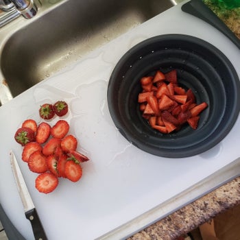 A reviewer photo of the cutting board over the sink with the built-in colander filled with strawberries 