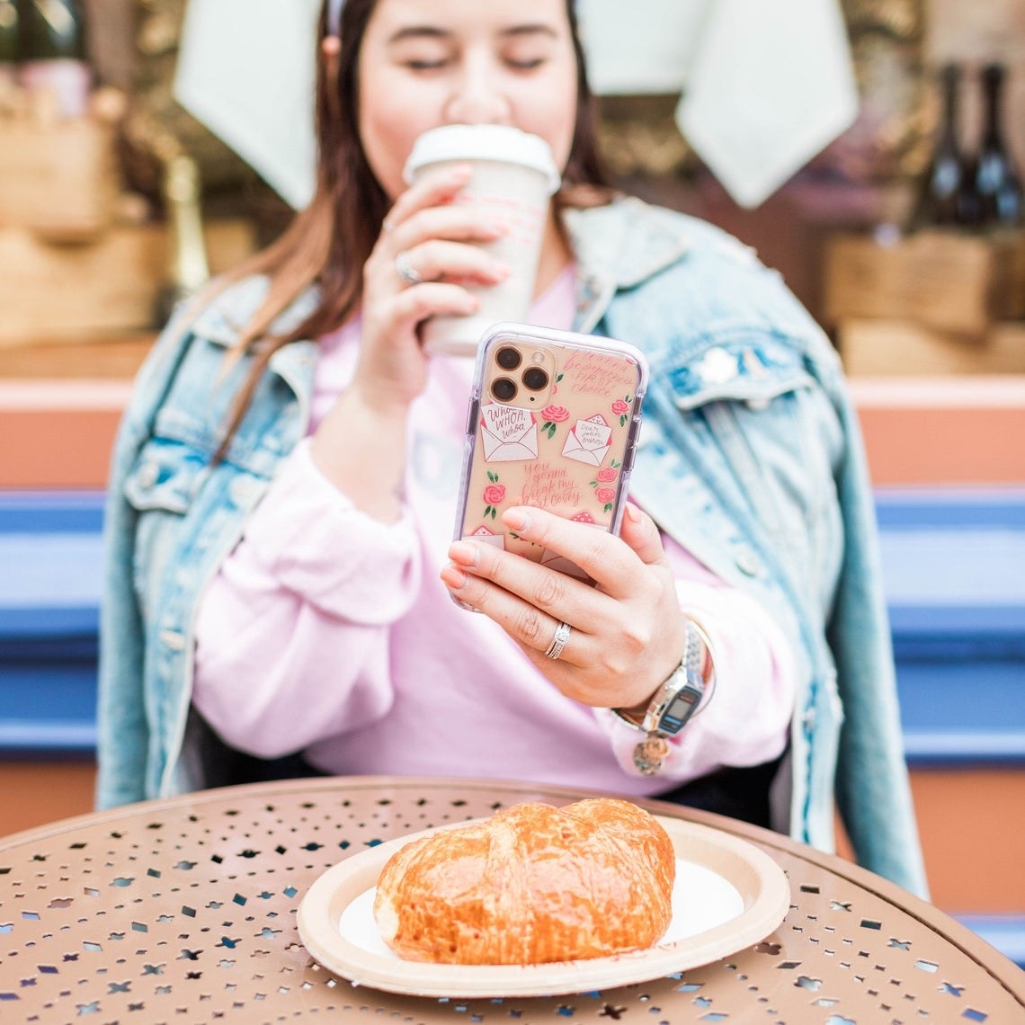 A person sitting at a table holding their phone up to take a picture of a pastry