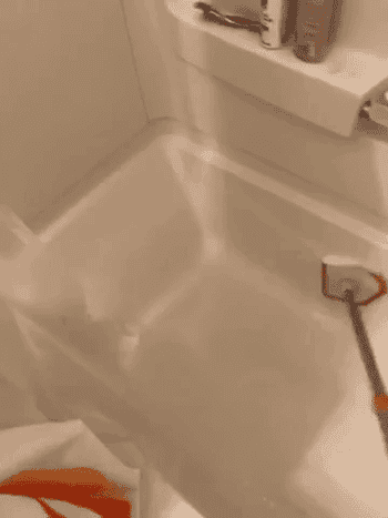 Reviewer using extendable scrubber to clean bathtub