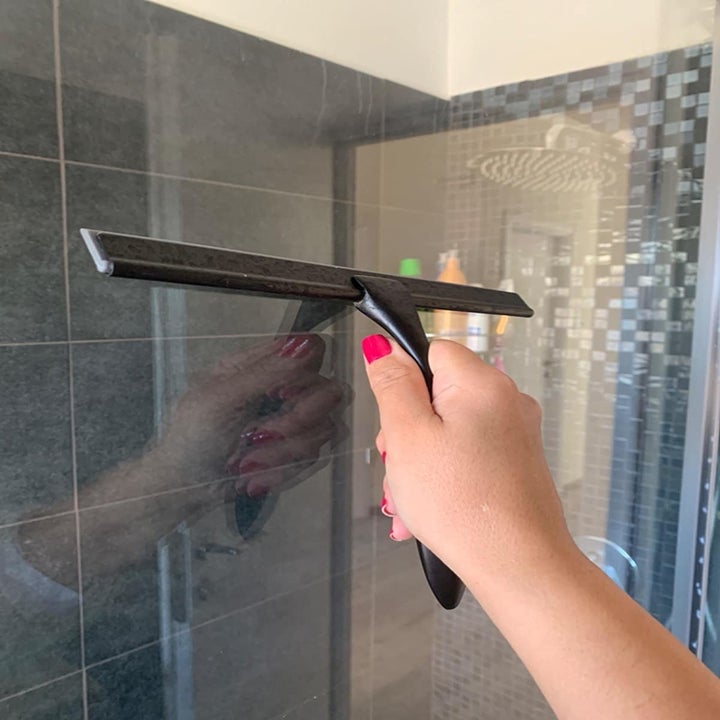 Reviewer using squeegee to wipe down glass shower wall