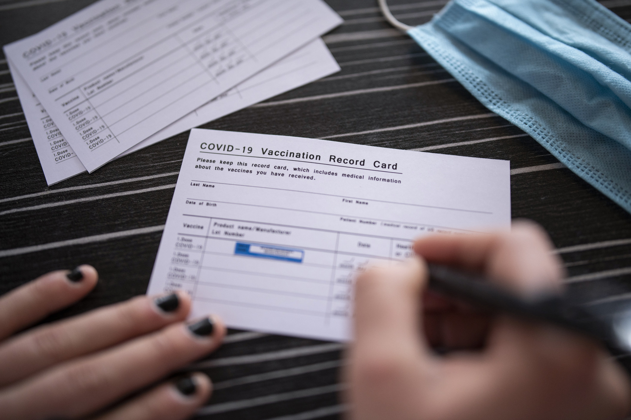 Doctor writing COVID-19 vaccination record card after vaccination on patient.