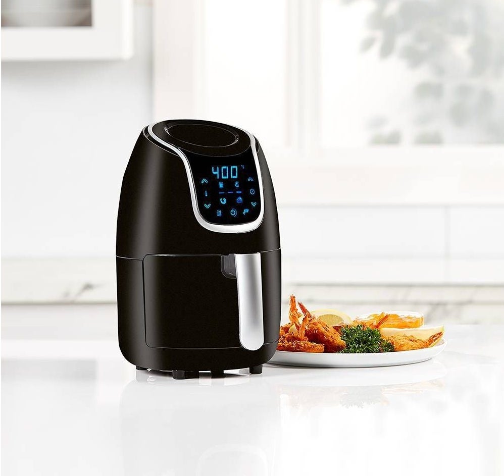The air fryer, which is small, black, and compact, with a large handle extending from the compartment where you place food