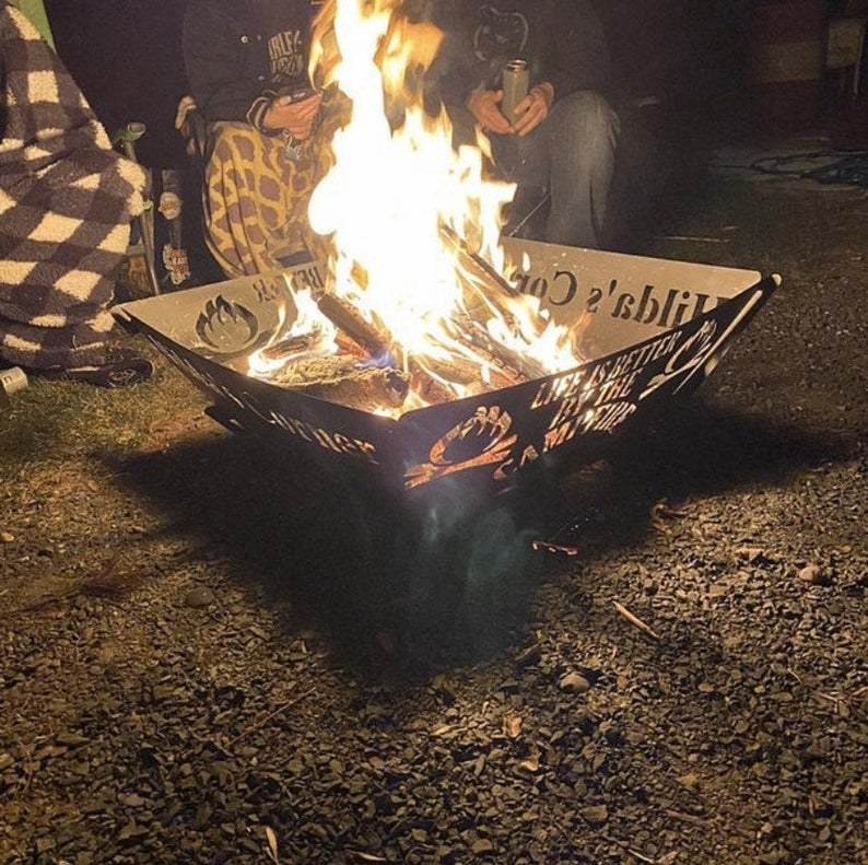 people sitting around the metal fire pit with a fire going at night