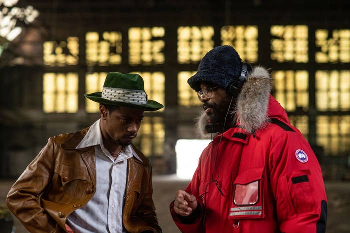 LaKeith Stanfield as William O'Neal wearing a greed fedora and tan leather jacket with Shaka King giving him directions on set