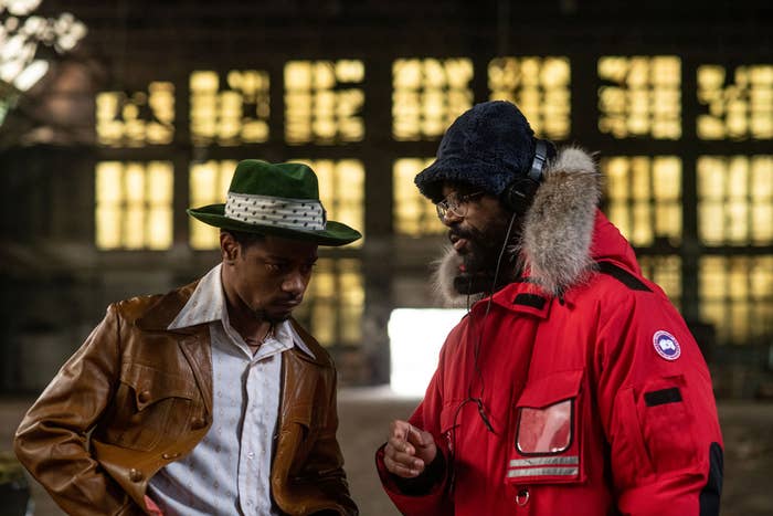 LaKeith Stanfield as William O&#x27;Neal wearing a greed fedora and tan leather jacket with Shaka King giving him directions on set