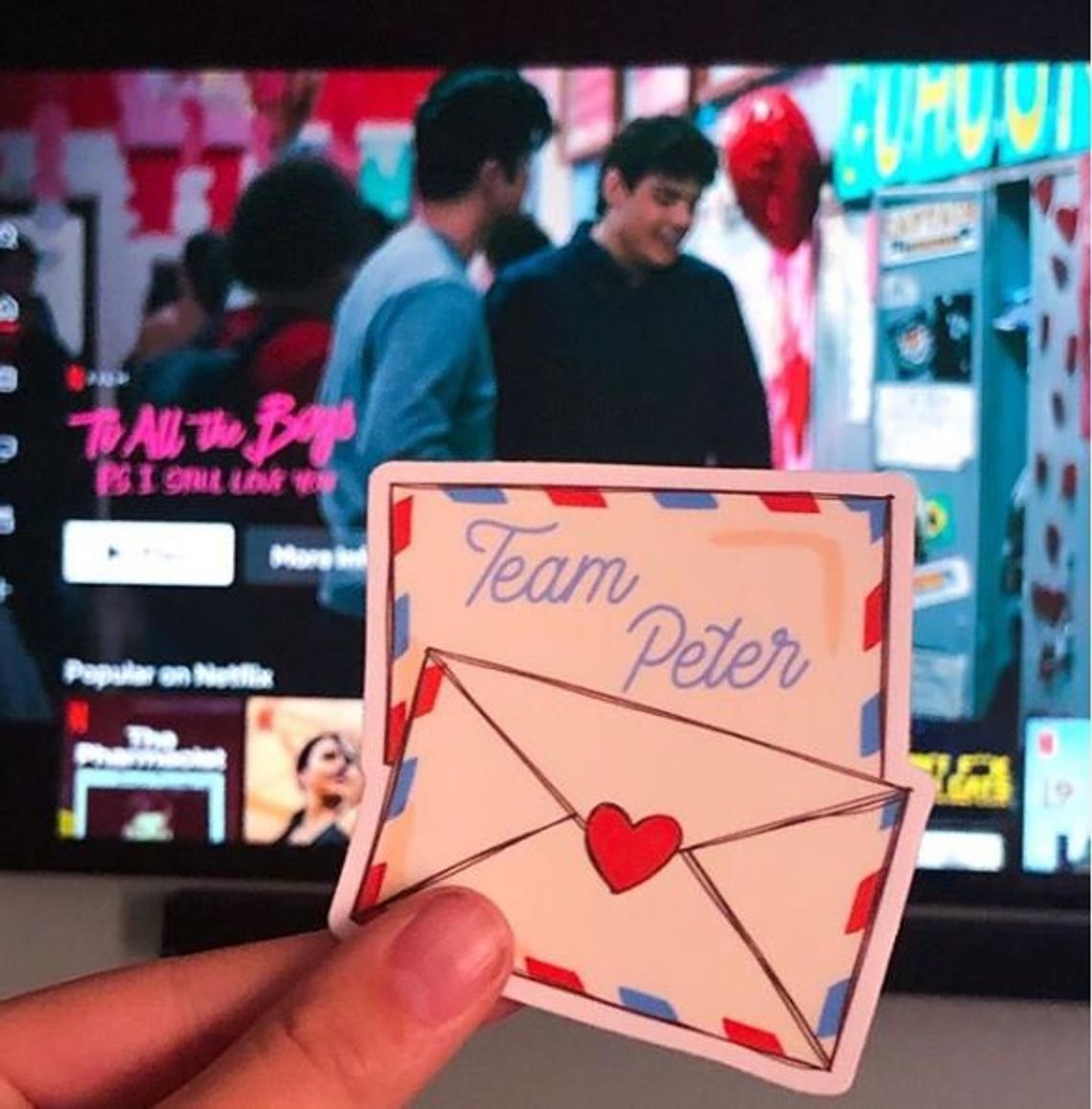 A person holding up a sticker of an envelope that says team Peter