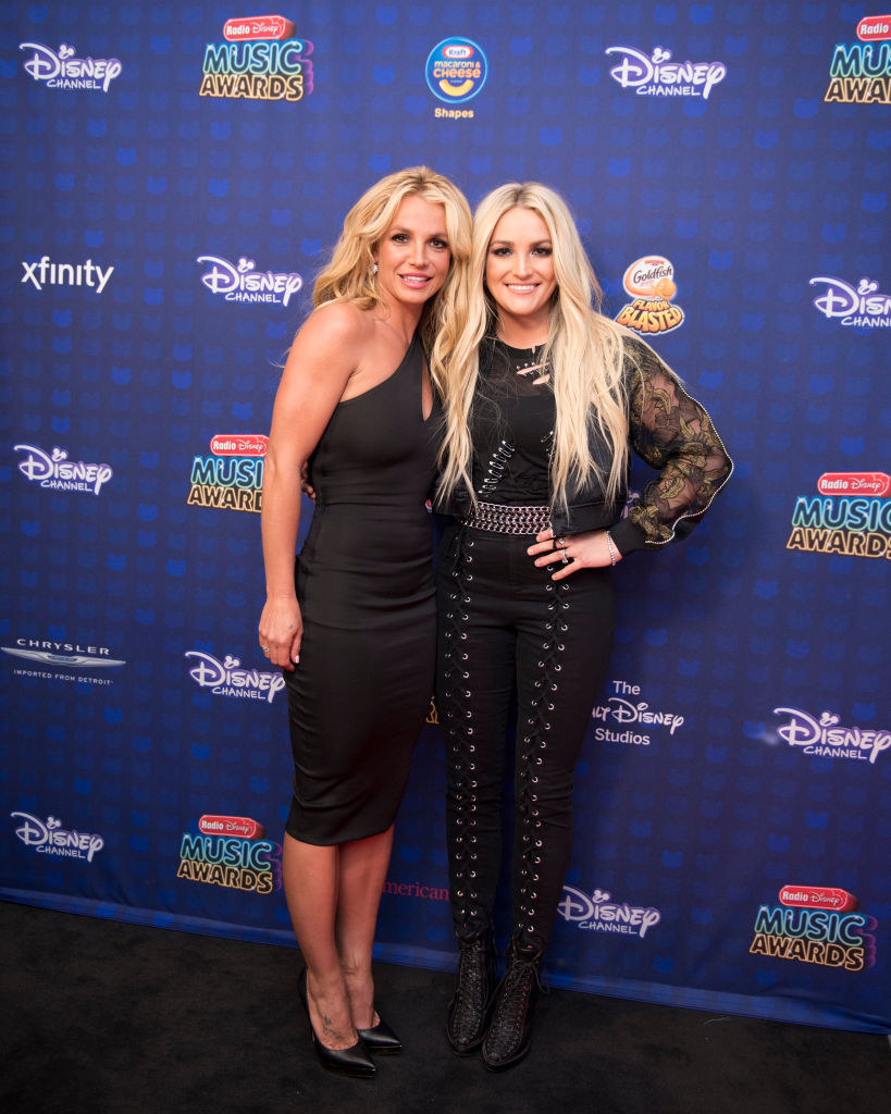 Britney, wearing a one-shouldered dress, and Jamie Lynn, wearing laced pants and a ripped top, posing at the Radio Disney Music Awards