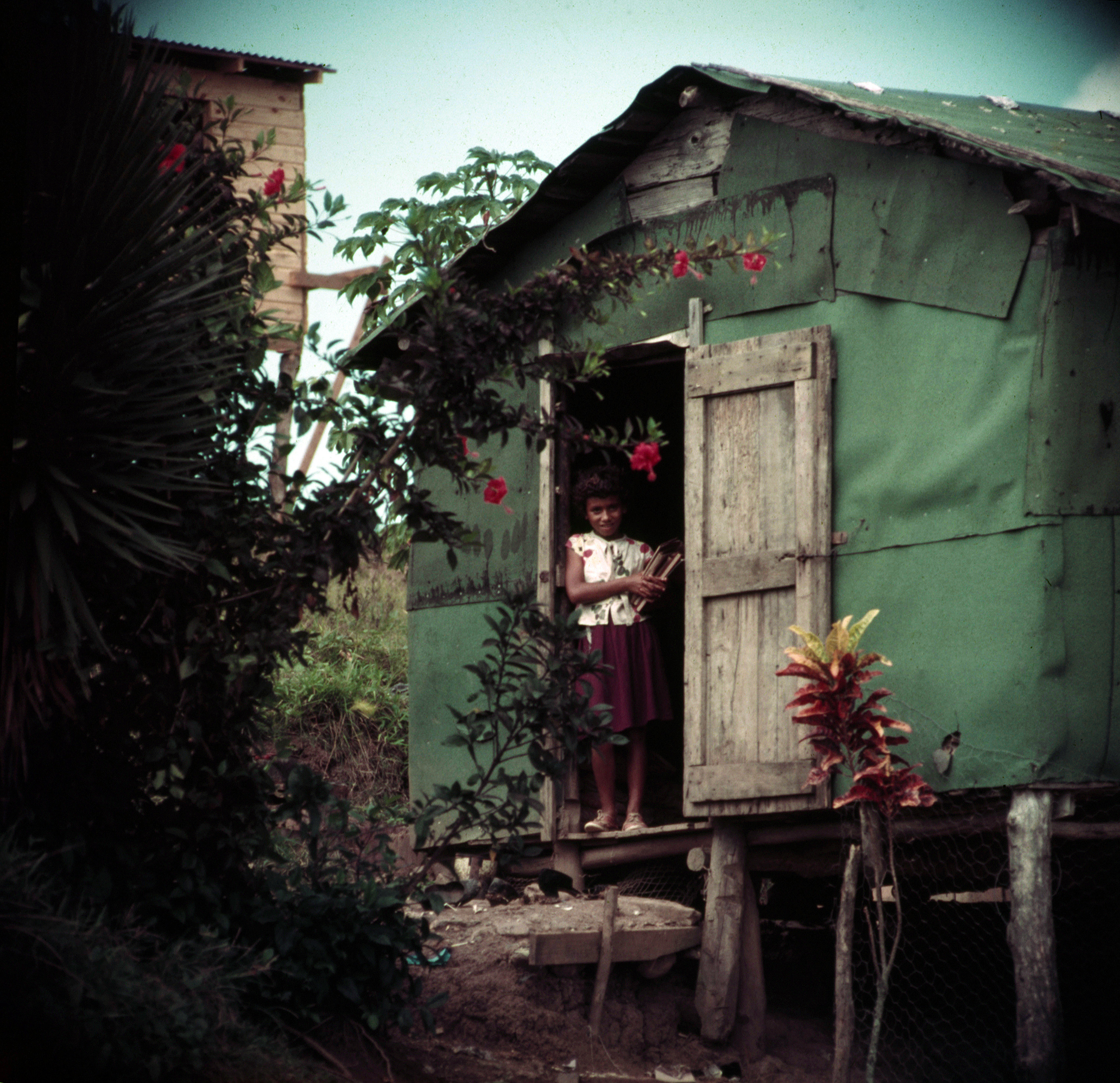 A young girl holding books at the entrance of a raised shack in Puerto Rico