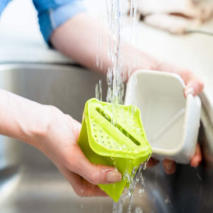 A pair of hand rinsing the soap holder portion of the caddy in the sink 