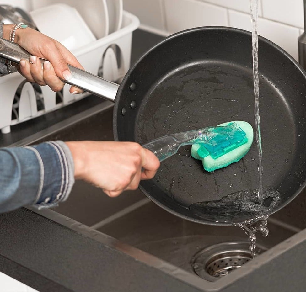 A person using the scrubber to clean a dirty frying pan