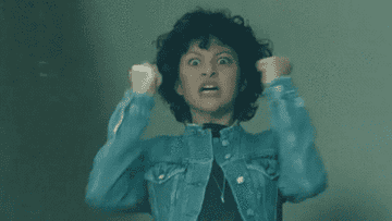 a woman in a jean jacket flails her arms around and makes her eyes wide as if angry 