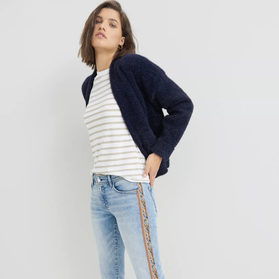 Model is wearing a dark blue cardigan, striped top, and denim pants