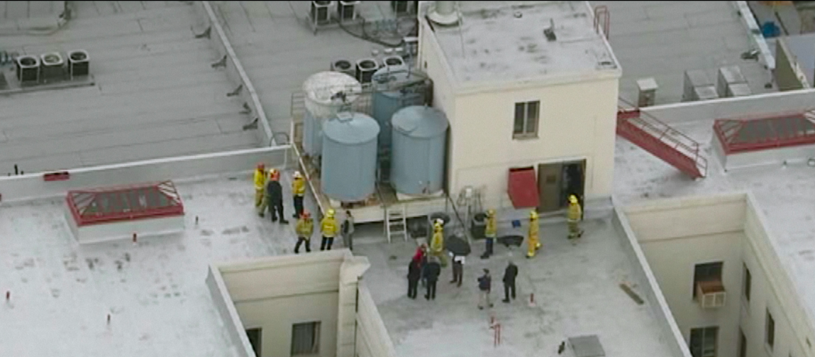 An aerial view of firefighters on a rooftop surrounding water tanks