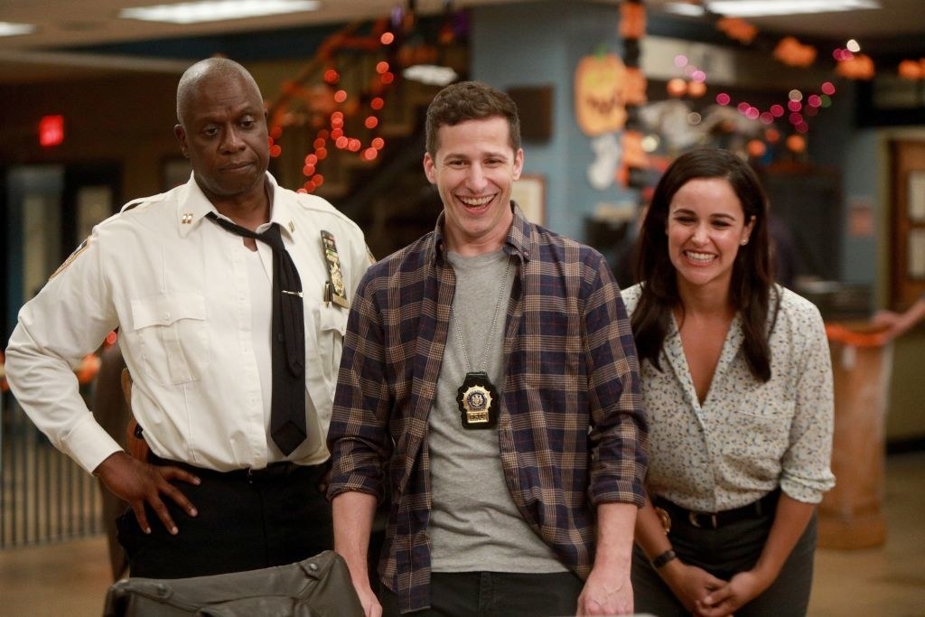 From left to right, Andre Braugher, Andy Samberg and Melissa Fumero standing next to each other as Andy and Melissa smile