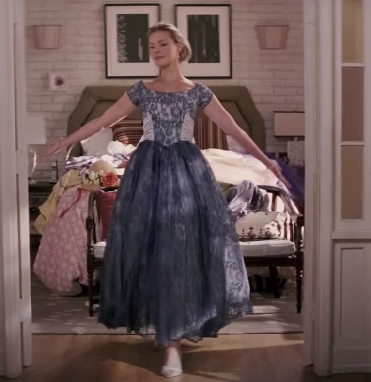 Jane wears an ankle length blue dress with lace overlay on the bodice