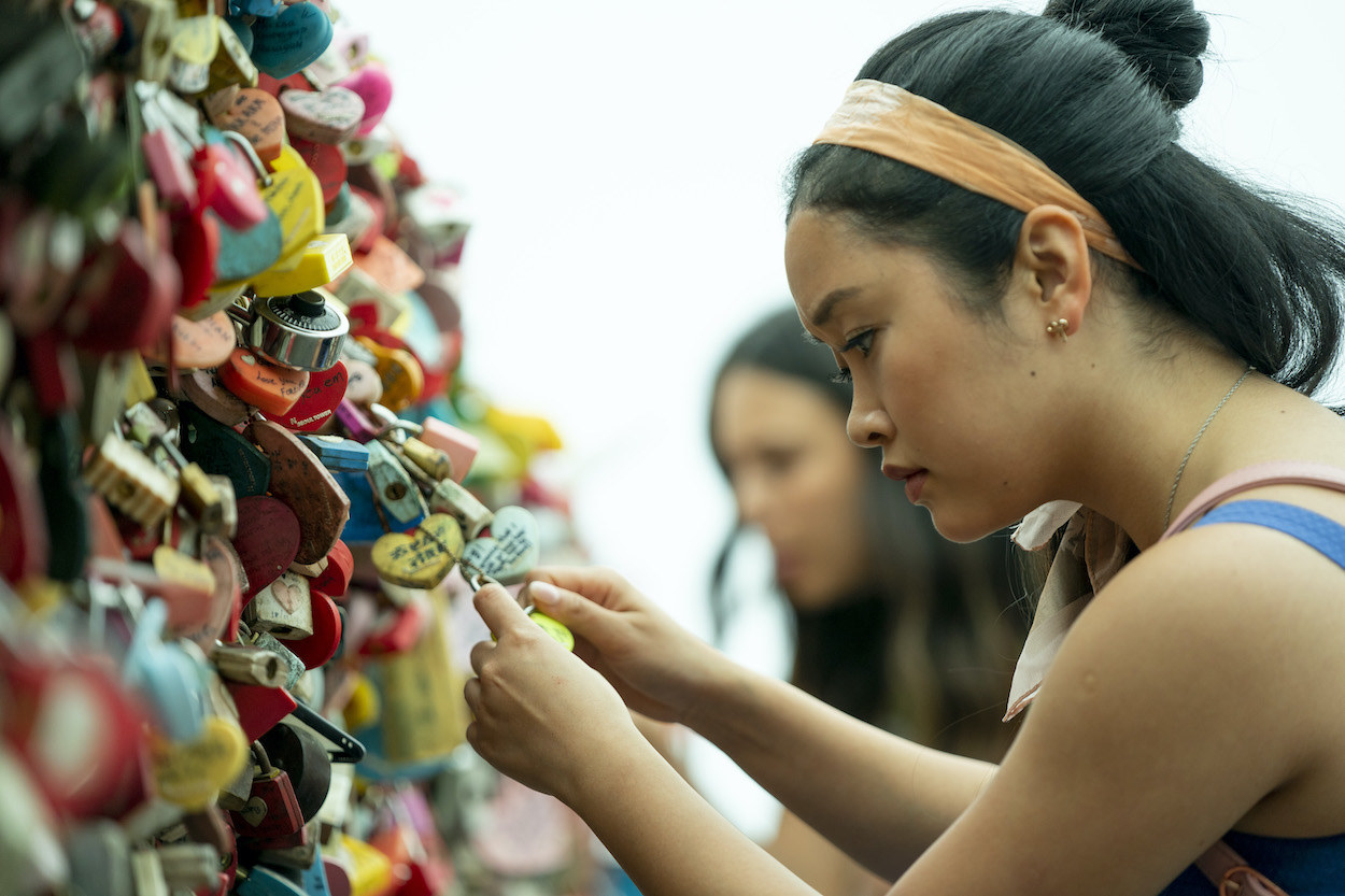 Lara Jean staring at a locket surrounded by hundreds of lockets on a fence