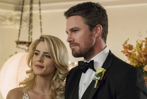 Felicity and Oliver stand side by side. She is smiling. He looks serious.