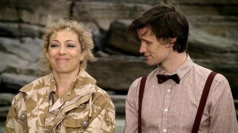 The Doctor looks at River Song while she smirks, amused.
