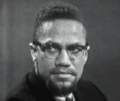 Malcolm X smiles in a black and white clip.