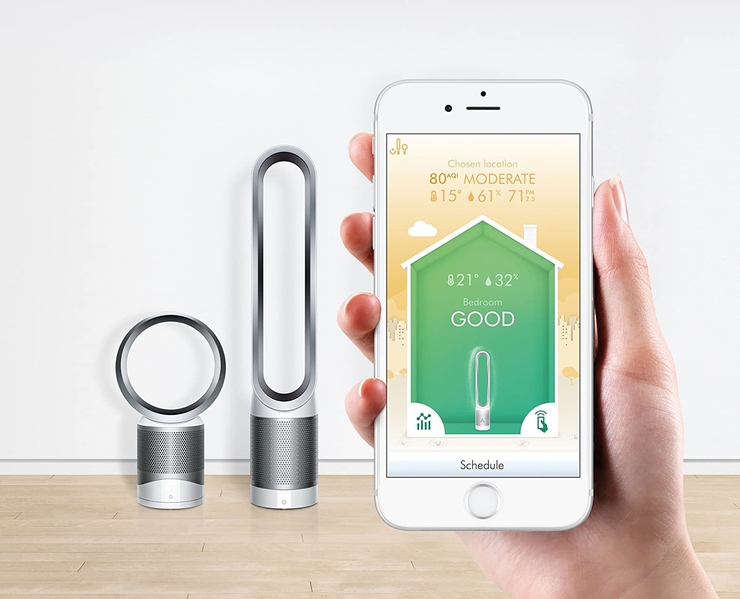 A Dyson Pure Cool Link Tower in front of a close up of a person holding a smartphone with the Dyson app open on it