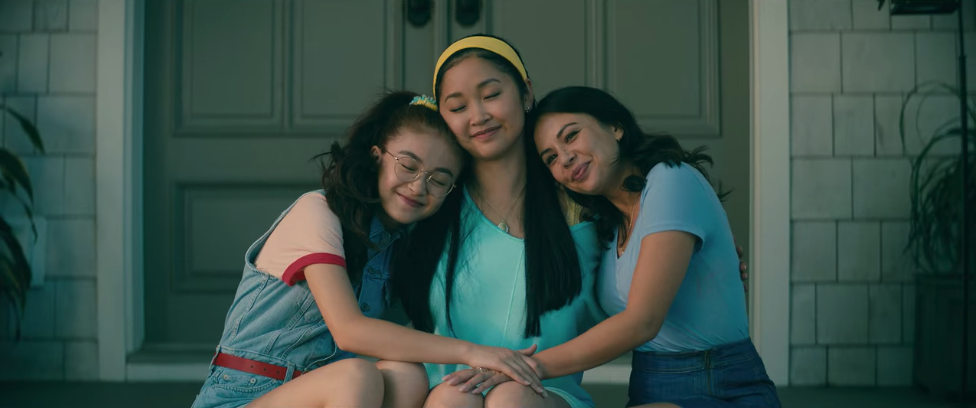 Kitty, Lara Jean and Margot hugging while sitting on their porch