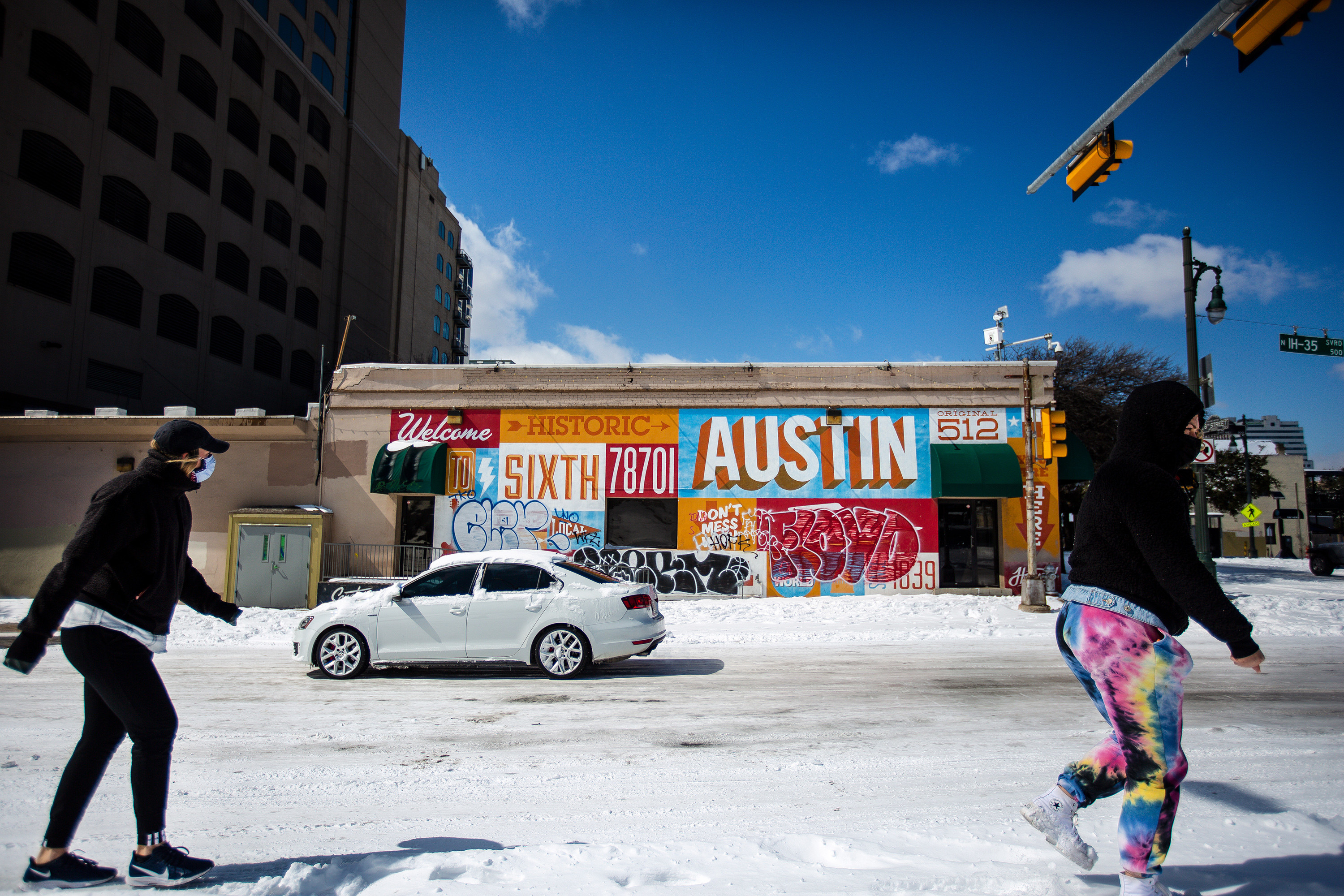 Two people walking past a mural in Austin Texas in the snow