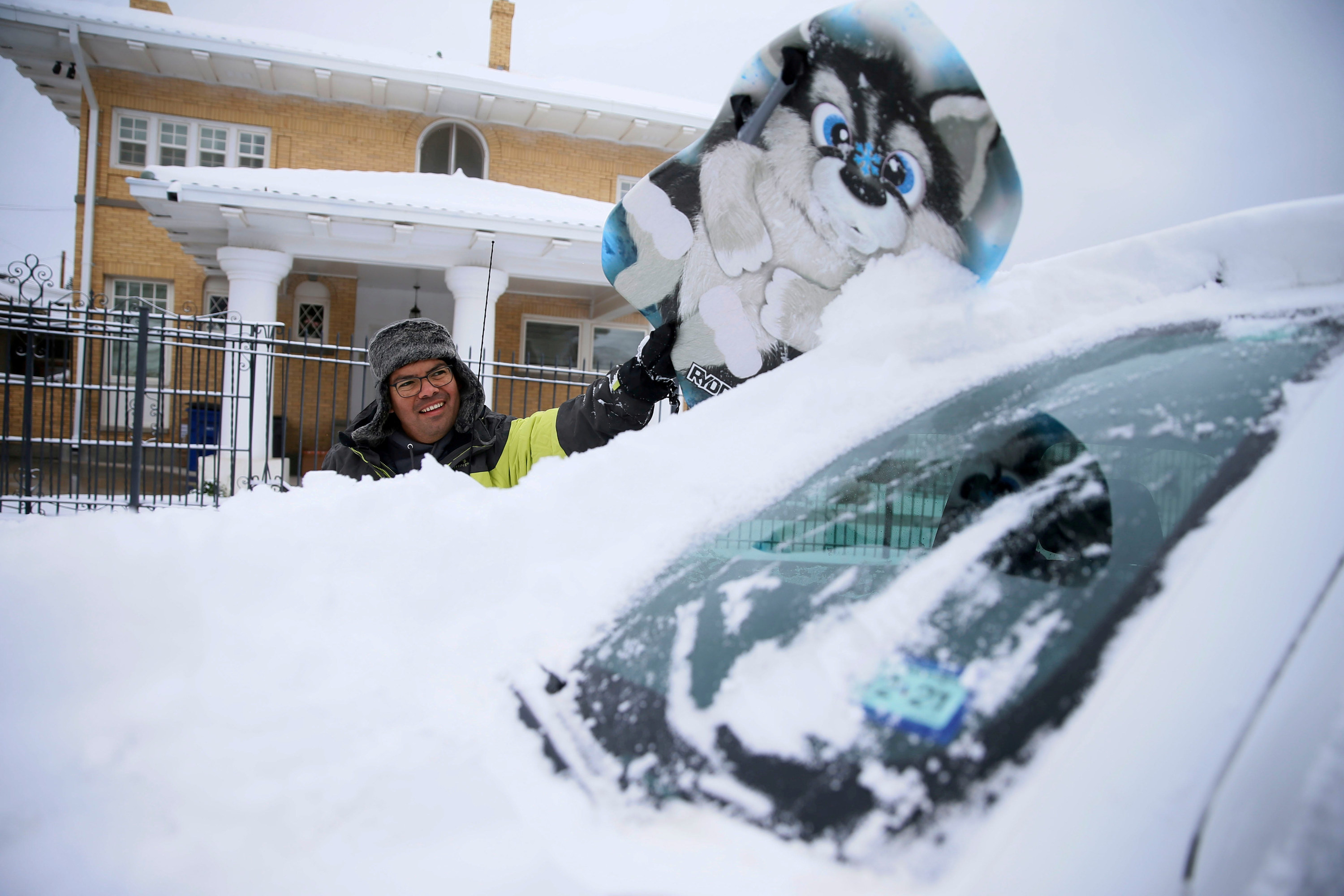 A smiling man cleaning snow off his car