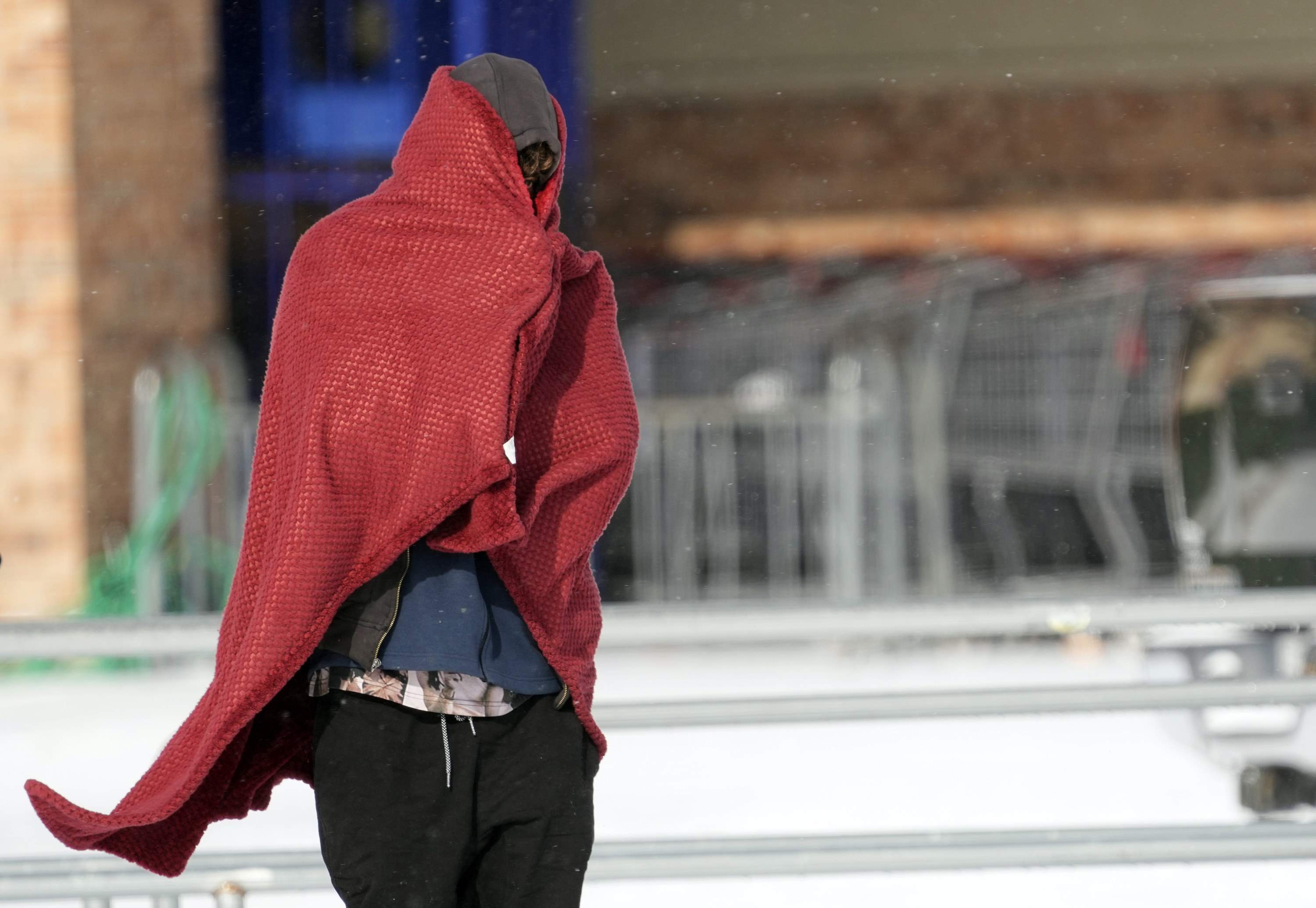 A man walks around with a sweatshirt and blanket to stay warm