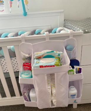 Reviewer image of caddy hung over a crib. It fits dozens of diapers, has a spot on top for wipes, and several pockets filled with varying baby items. 