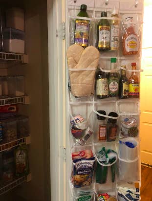 Reviewer's pantry with clear pockets hanging over the door. There are five levels with pockets filled to the brim with bottles, seasoning, and other kitchen tools. 