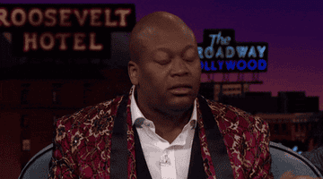 Tituss Burgess leans back with wide eyes in shock and looks around on The Late Late Show With James Corden