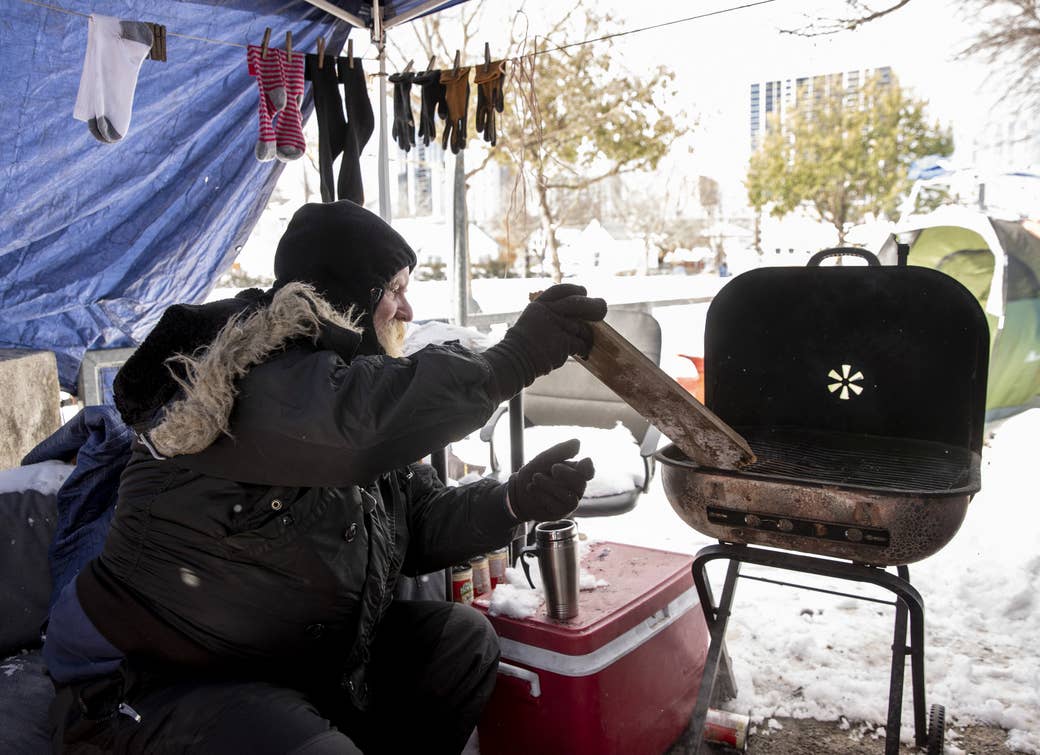 A homeless man uses a grill for heat