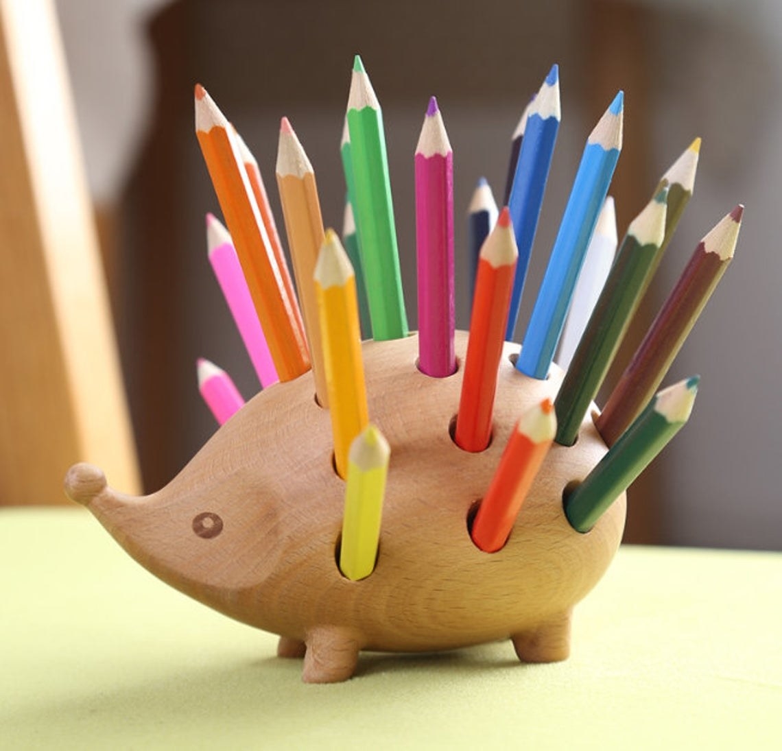 Wooden hedgehog with holes holding several colored pencils on its back 