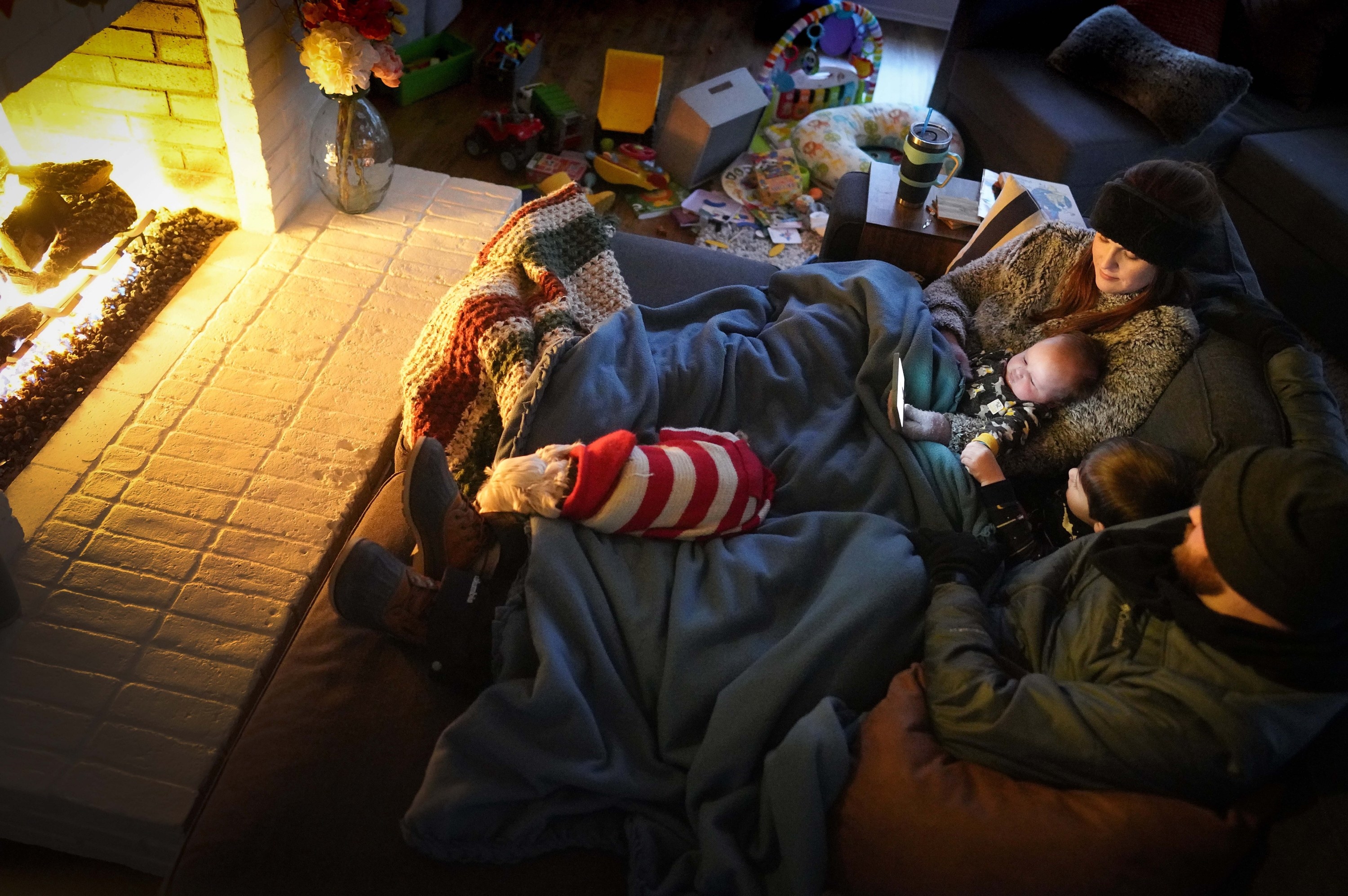 A family curls up around the fire indoors