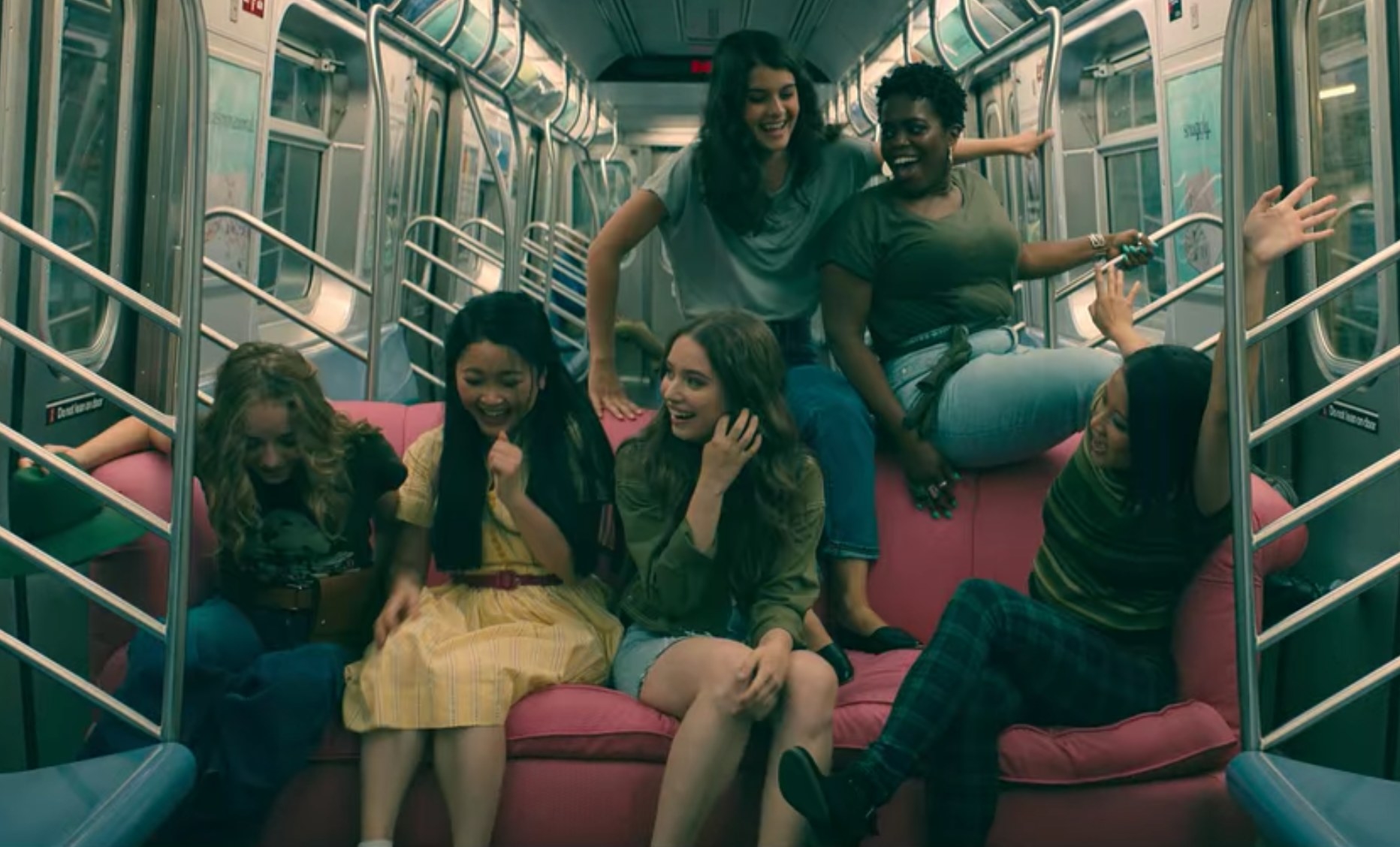 Lara Jean and friends sit on a couch inside of a subway train